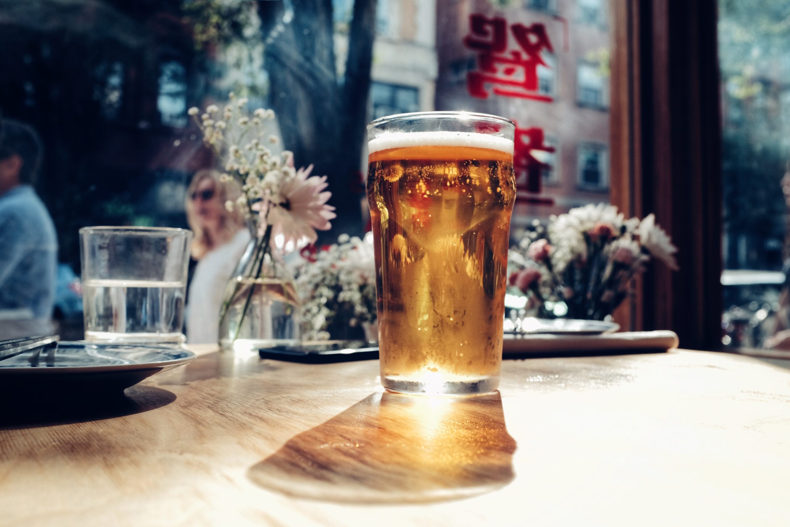 image of a pint of lager with flowers in the background